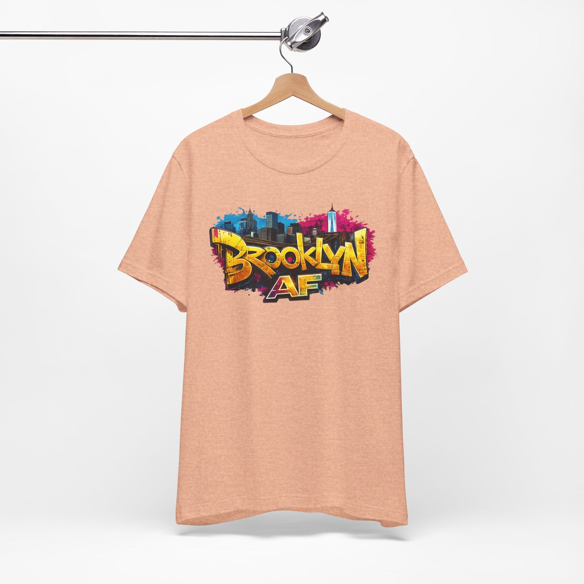 Heather Peach t-shirt on a wooden hanger, front view, with graffiti-style Brooklyn AF lettering over a skyline splash.