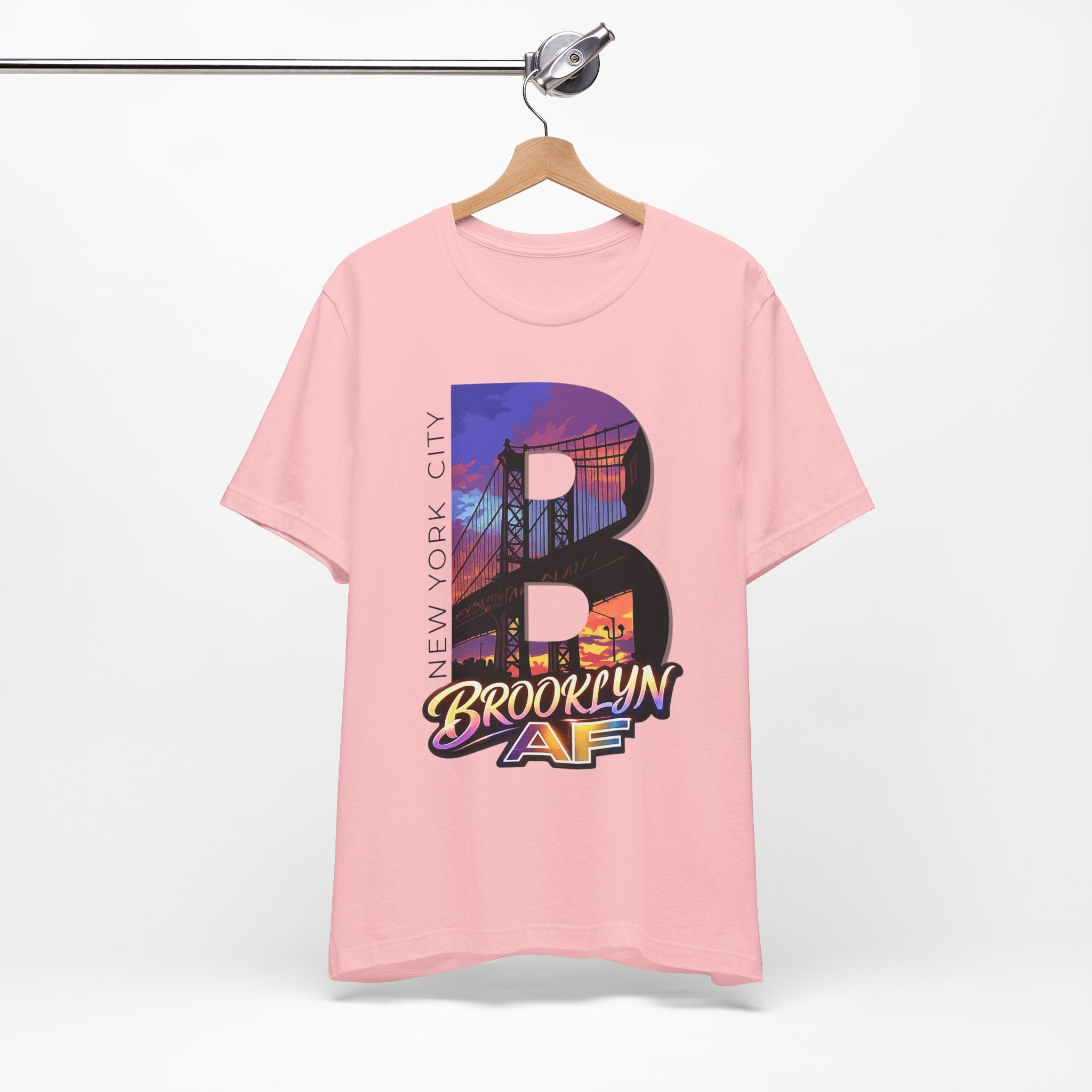 Pink tee on a hanger, front view, showing the oversized "B" Brooklyn Bridge sunset skyline graphic and logo.