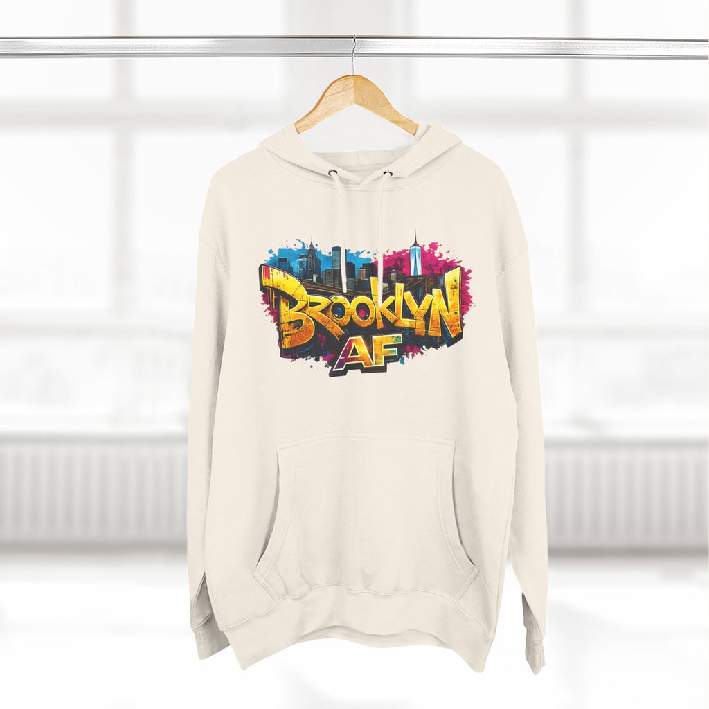 Pale Pink hoodie hanging on a wooden hanger, showing the colorful graffiti-style Brooklyn AF skyline print.