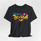 Black t-shirt, front view flat lay, showing graffiti Brooklyn AF lettering over a skyline with paint-splash design.