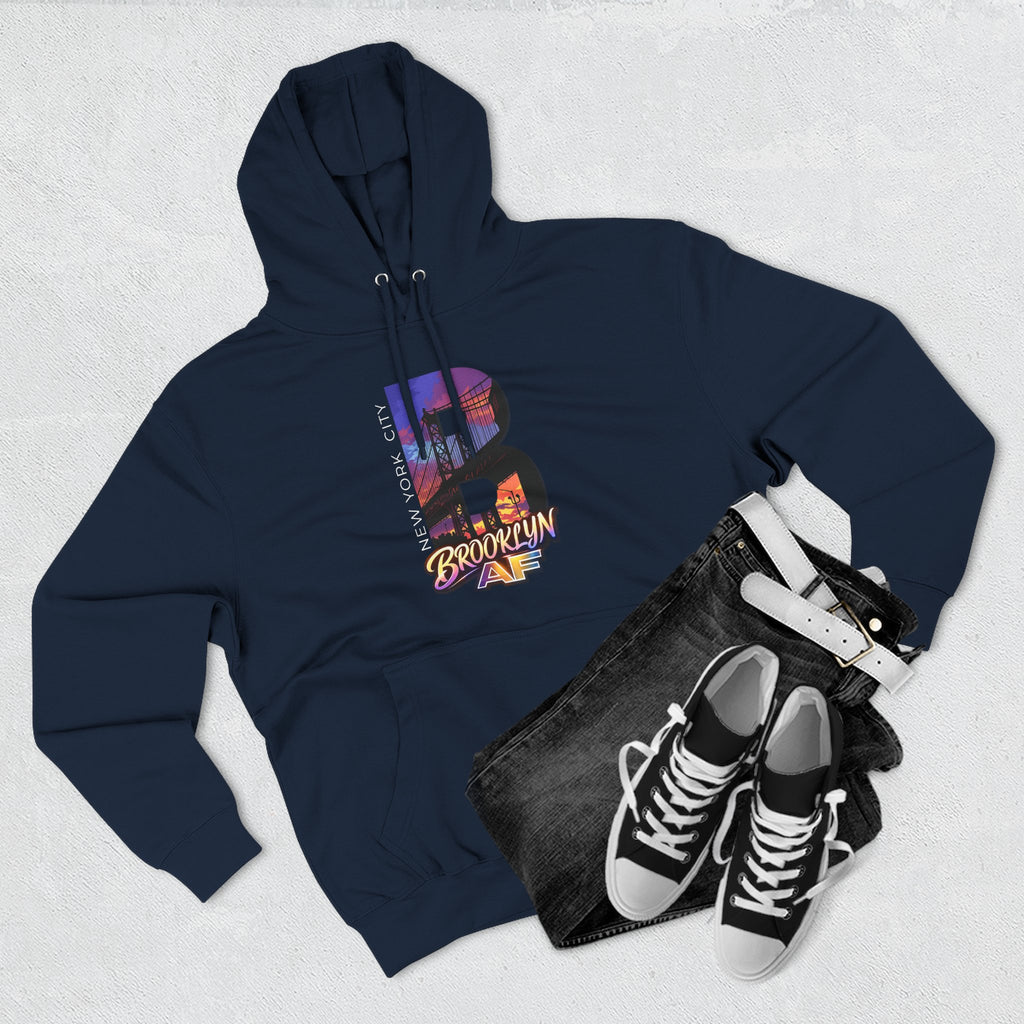 Navy hoodie flat lay styled with jeans, white belt, and sneakers, showing the oversized "B" Brooklyn Bridge skyline graphic.