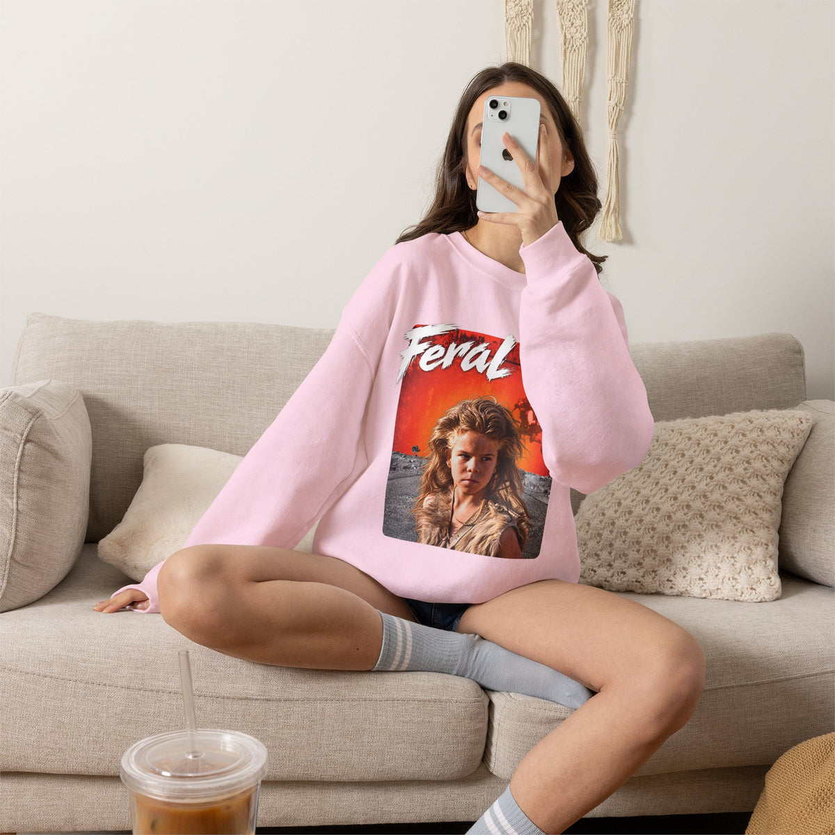 Woman sitting on a sofa in the Light Pink Feral AF sweatshirt, wasteland graphic on show