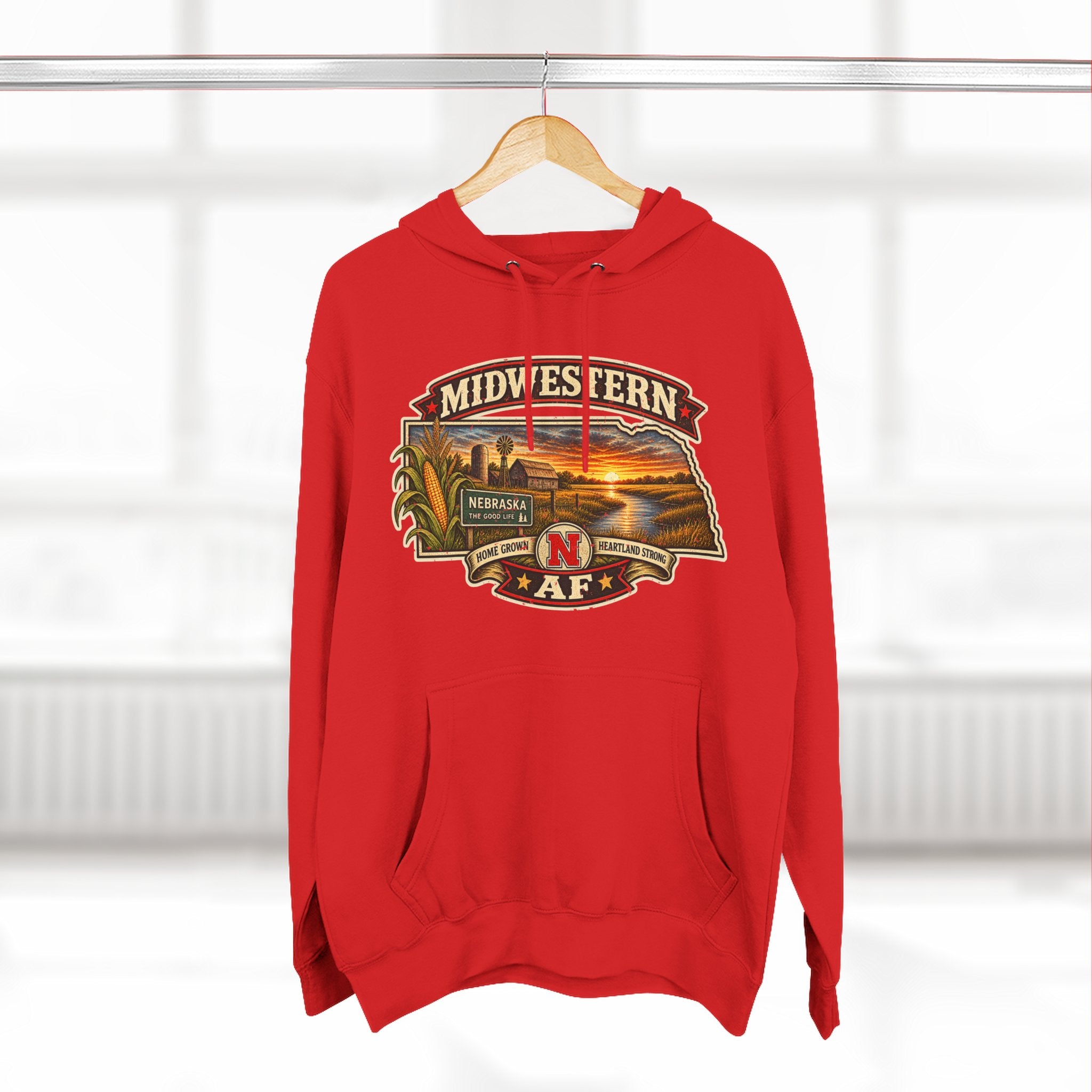 Red Nebraska hoodie on a wooden hanger by a bright window, front print facing forward