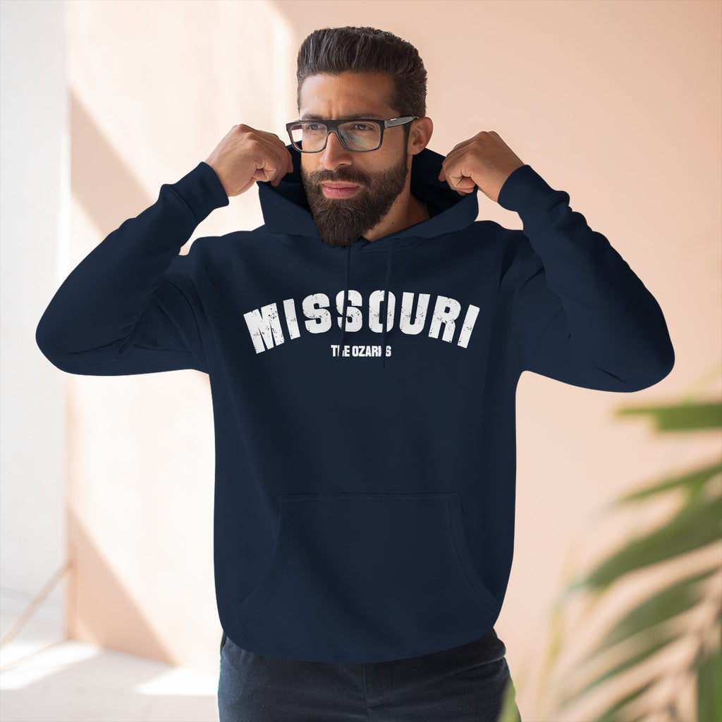 Bearded man pulling up the hood of the navy Missouri hoodie printed MISSOURI over THE OZARKS