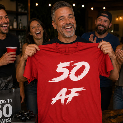 Man at an outdoor party holding up the red 50 AF birthday tee while friends laugh behind him