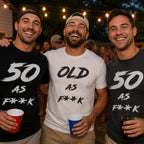 Three men at an outdoor party under string lights in black, white and dark grey 50 AS F**K and OLD AS F**K tees