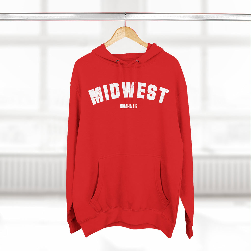 Red custom Midwest hoodie hanging on a wooden hanger by a window