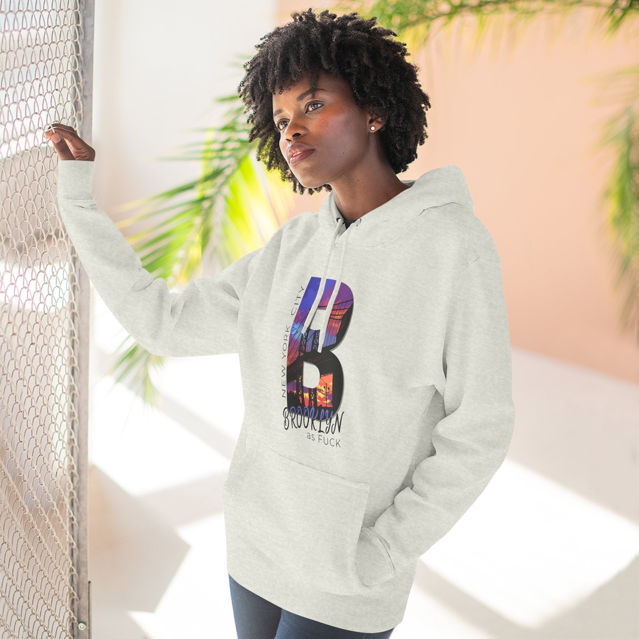 Heather grey hoodie worn by a model outdoors near a fence, alternate shot, showing the 'B' Brooklyn skyline graphic.