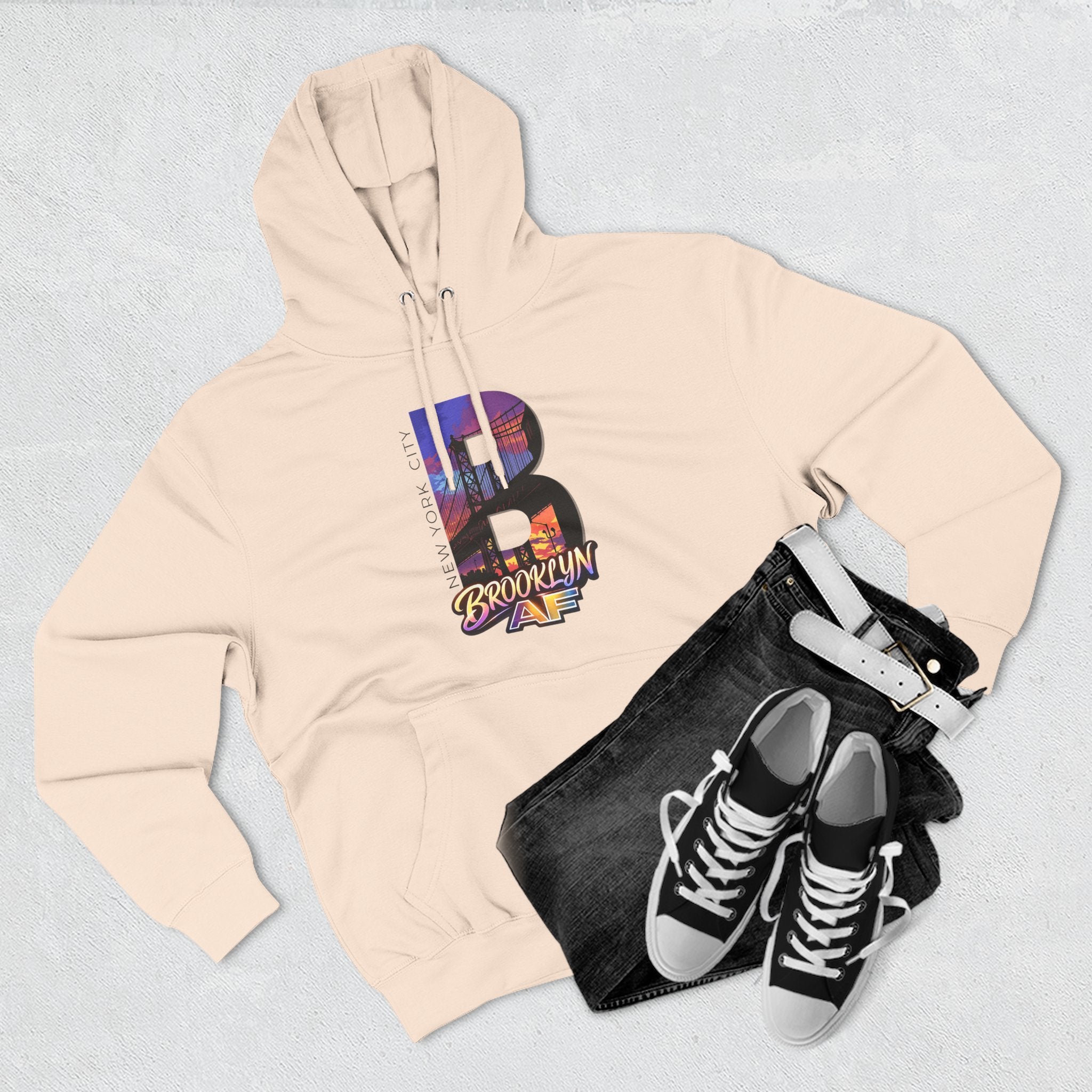 Oatmeal heather hoodie styled with black jeans, belt, and sneakers, bold B featuring a Brooklyn Bridge skyline graphic.