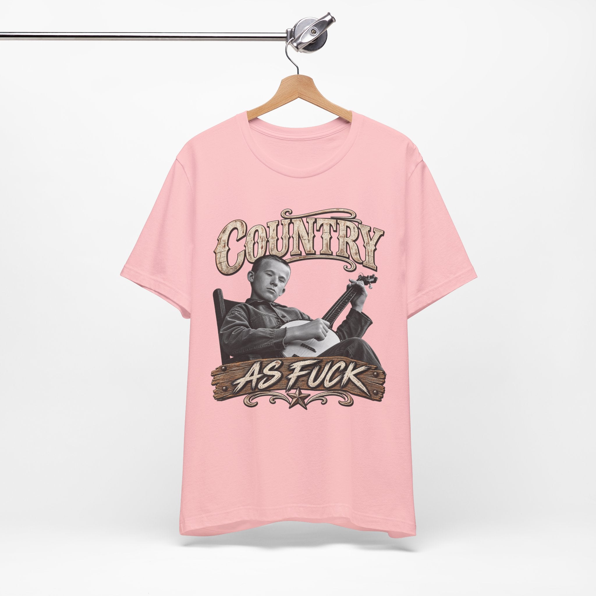 Pink Country As Fuck tee on a wooden hanger, banjo front print showing