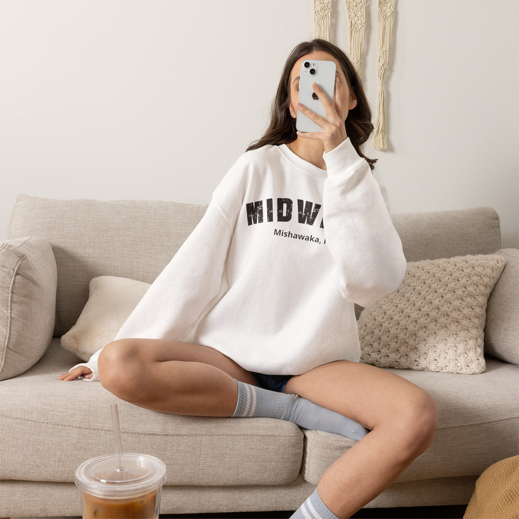 Woman on a sofa in the White custom Midwest crewneck, hometown text under the varsity lettering