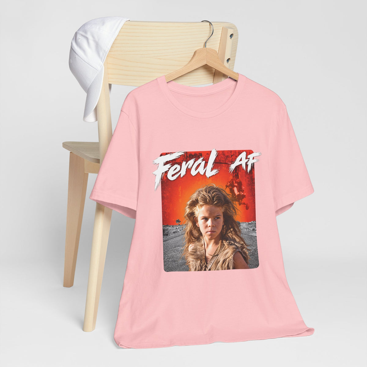 Pink Feral AF tee draped over a light wooden chair, front graphic facing forward