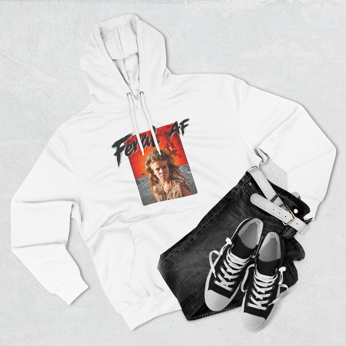 White Feral AF hoodie styled flat with jeans and canvas sneakers on a pale backdrop
