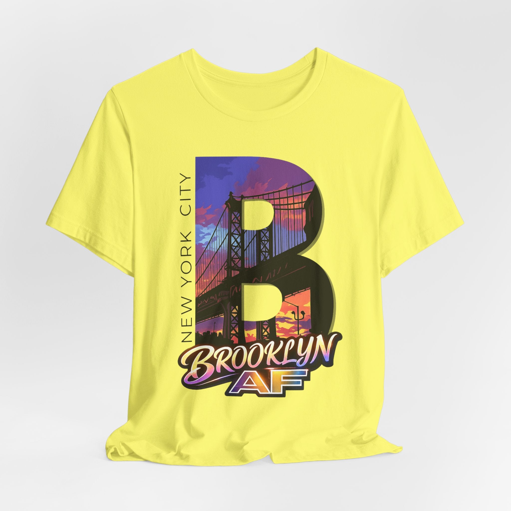 Yellow t-shirt flat lay, front view with full 'B' graphic, Brooklyn Bridge sunset skyline and 'Brooklyn AF' logo