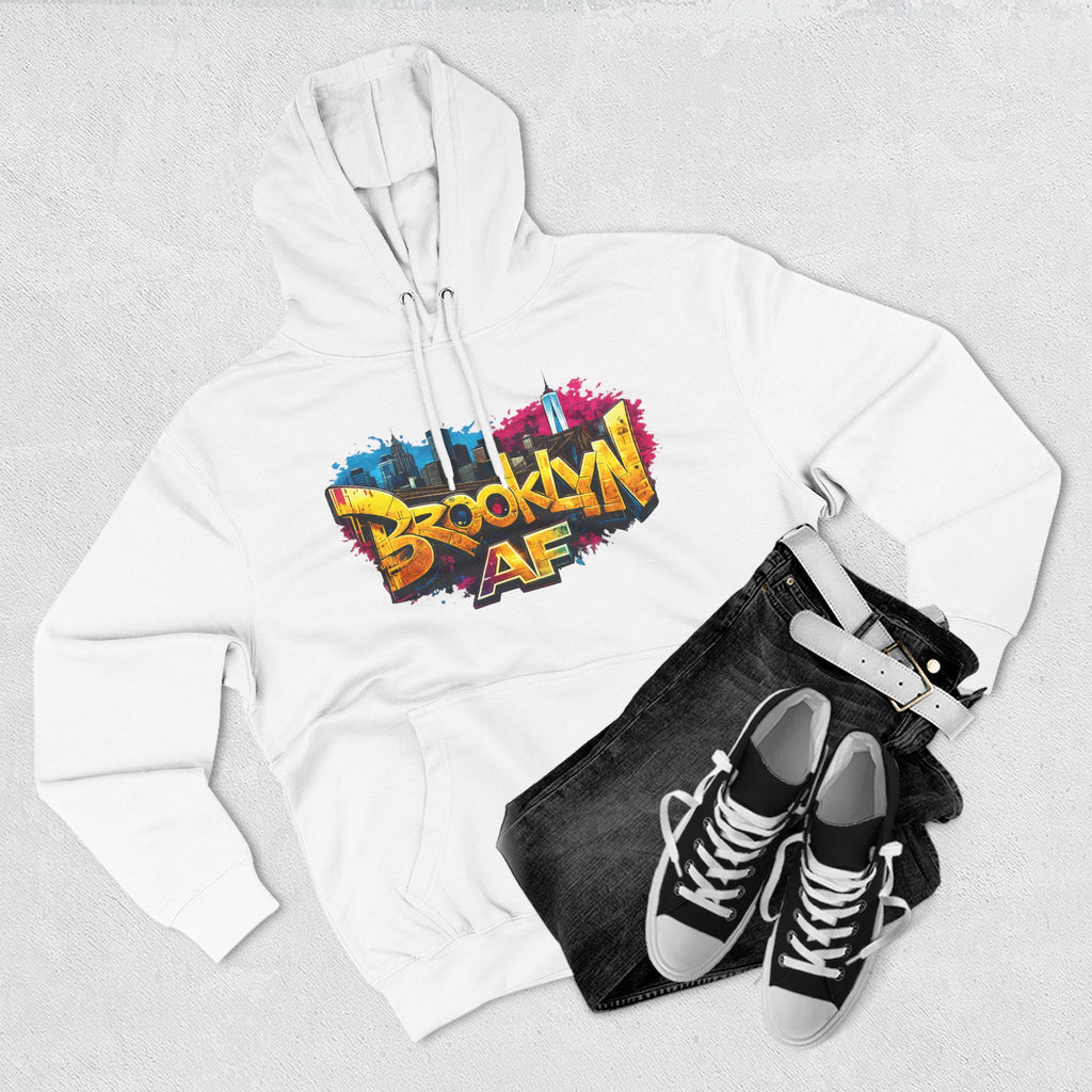White hoodie flat lay styled with black jeans and sneakers, showing the graffiti-style Brooklyn AF skyline print.