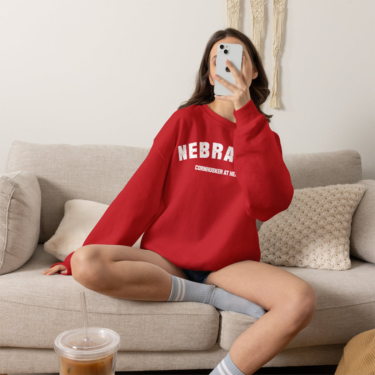 Woman on a couch wearing the Red personalized Nebraska sweatshirt with distressed varsity lettering