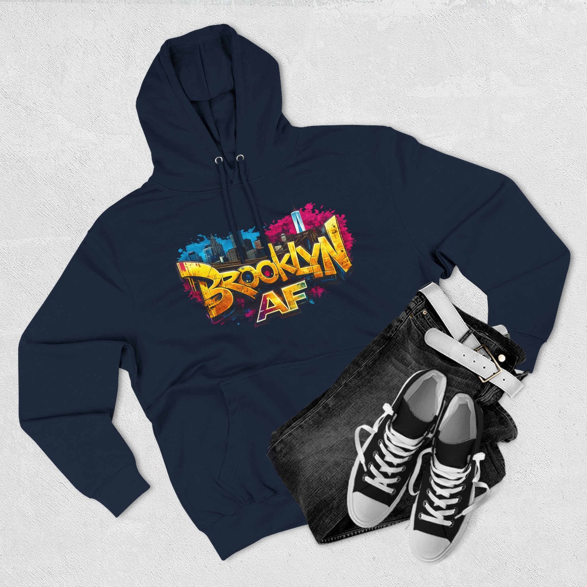 Navy hoodie flat lay styled with black jeans and sneakers, showing the graffiti-style Brooklyn AF skyline print.