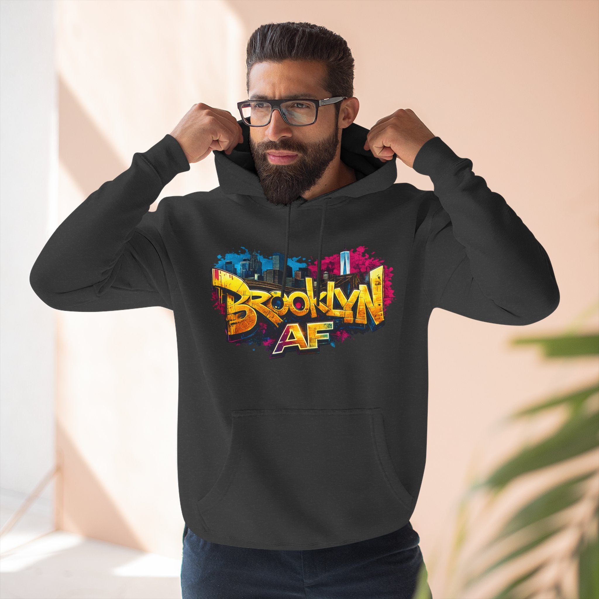 Black hoodie worn by a male model adjusting the hood, close-up front view of the graffiti-style Brooklyn AF print.