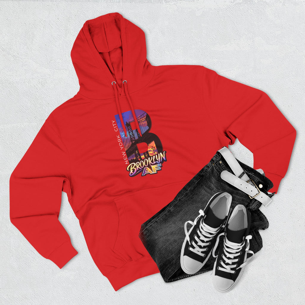 Red hoodie flat lay styled with jeans and sneakers, featuring the oversized B Brooklyn Bridge skyline graphic.