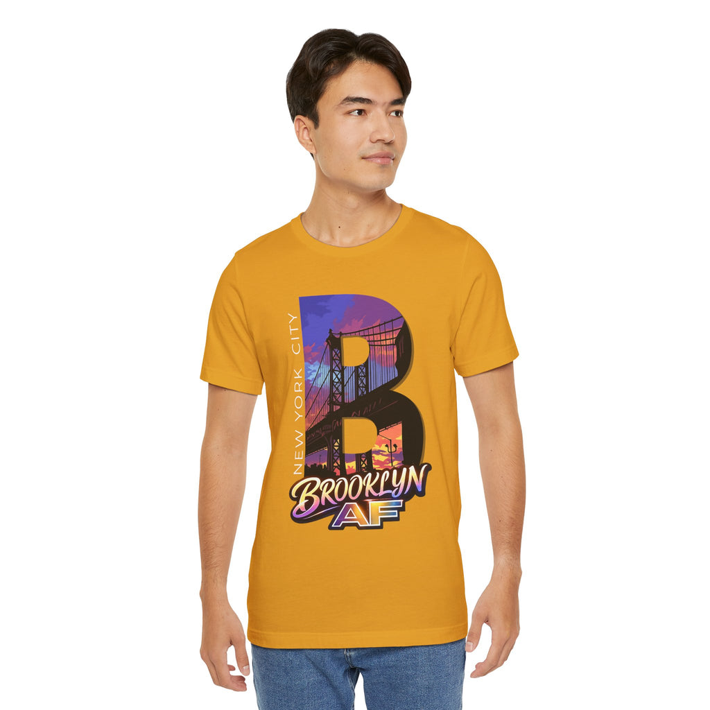 Mustard yellow t-shirt worn by a male model, front view, with a bold B and purple-orange Brooklyn Bridge sunset graphic.