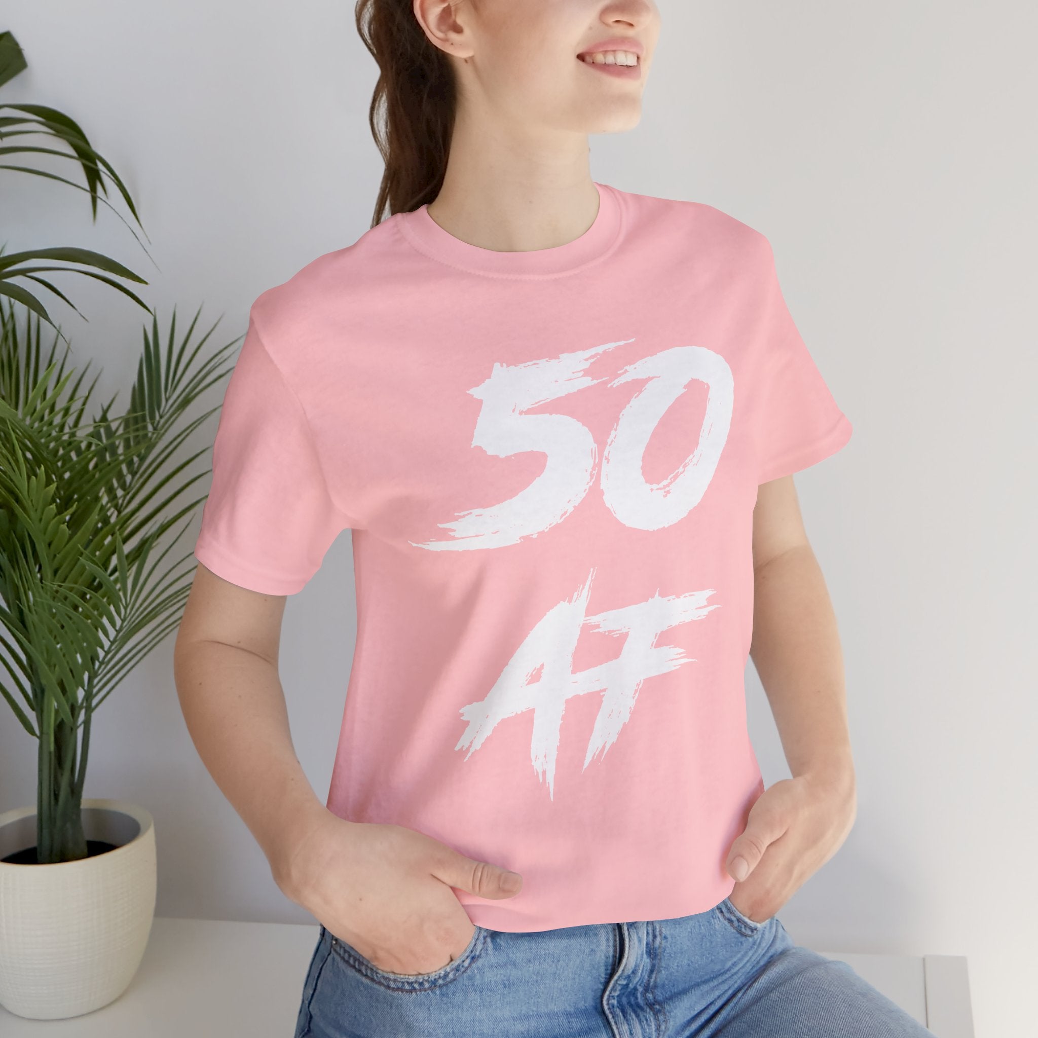 Woman in the pink 50 AF birthday tee photographed indoors next to a houseplant