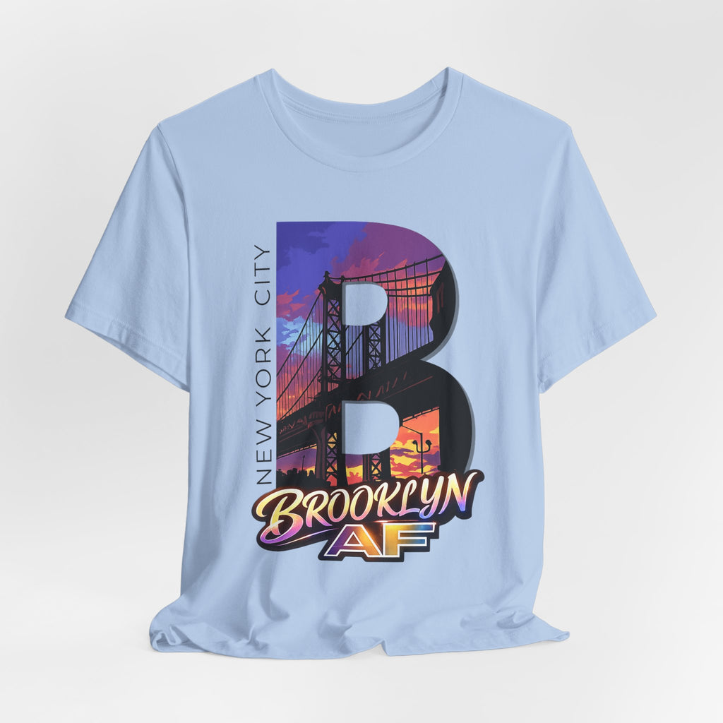 Light blue t-shirt flat lay, front view with full 'B' graphic, Brooklyn Bridge sunset skyline and 'Brooklyn AF' logo