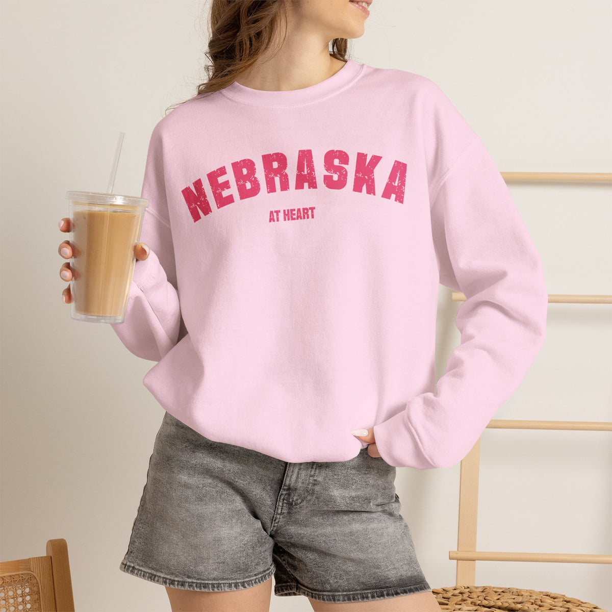 Light Pink Nebraska sweatshirt worn with an iced coffee, pink varsity lettering above AT HEART