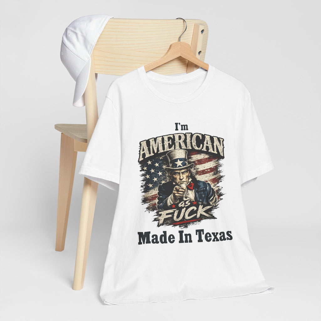 White tee hanging on a chair with a cap, Uncle Sam graphic and "I'm American As Fuck, Made In Texas" text