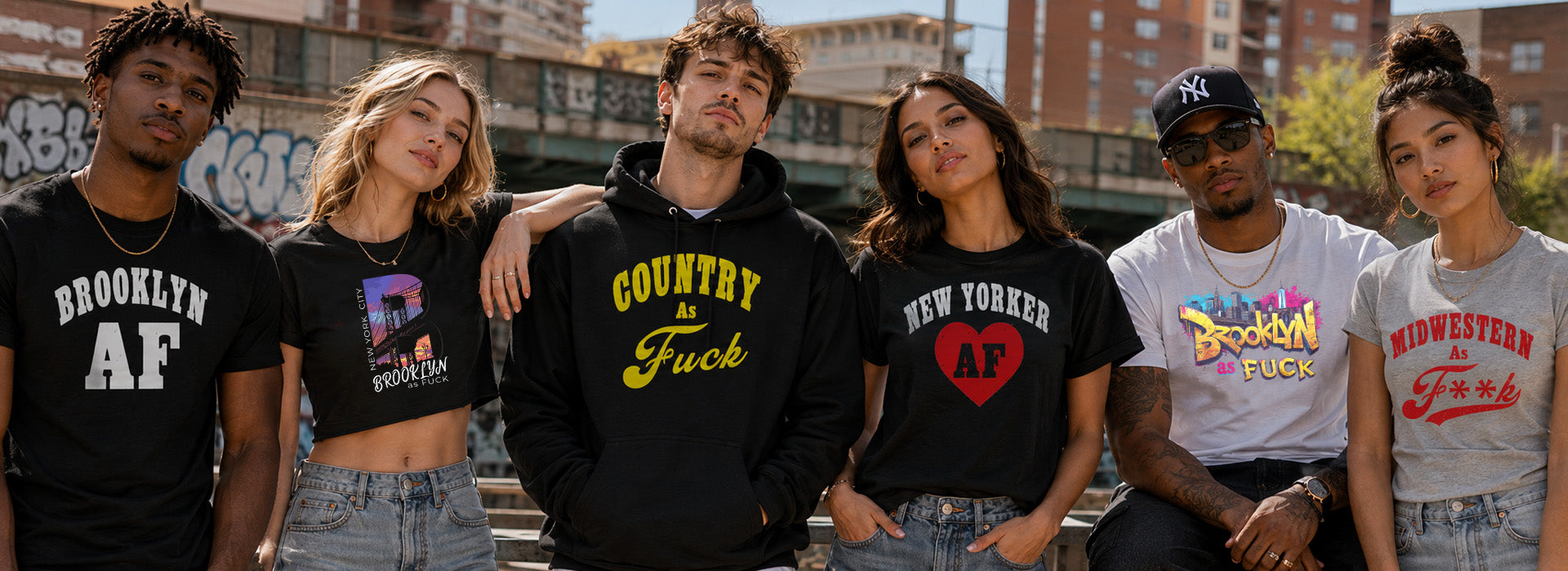 Six young adults standing together outdoors in front of brick buildings, each wearing a graphic T-shirt. The shirts feature collegiate-style designs including 'BROOKLYN AF', 'COUNTRY F*CK', 'NEW YORKER AF', 'BROOKLYN F*CK', and 'MICHIGAN F*CK'.