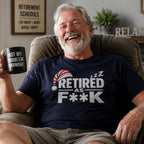 Laughing retiree in a recliner wearing the navy Retired As F**K tee, holding a Not My Problem Anymore mug