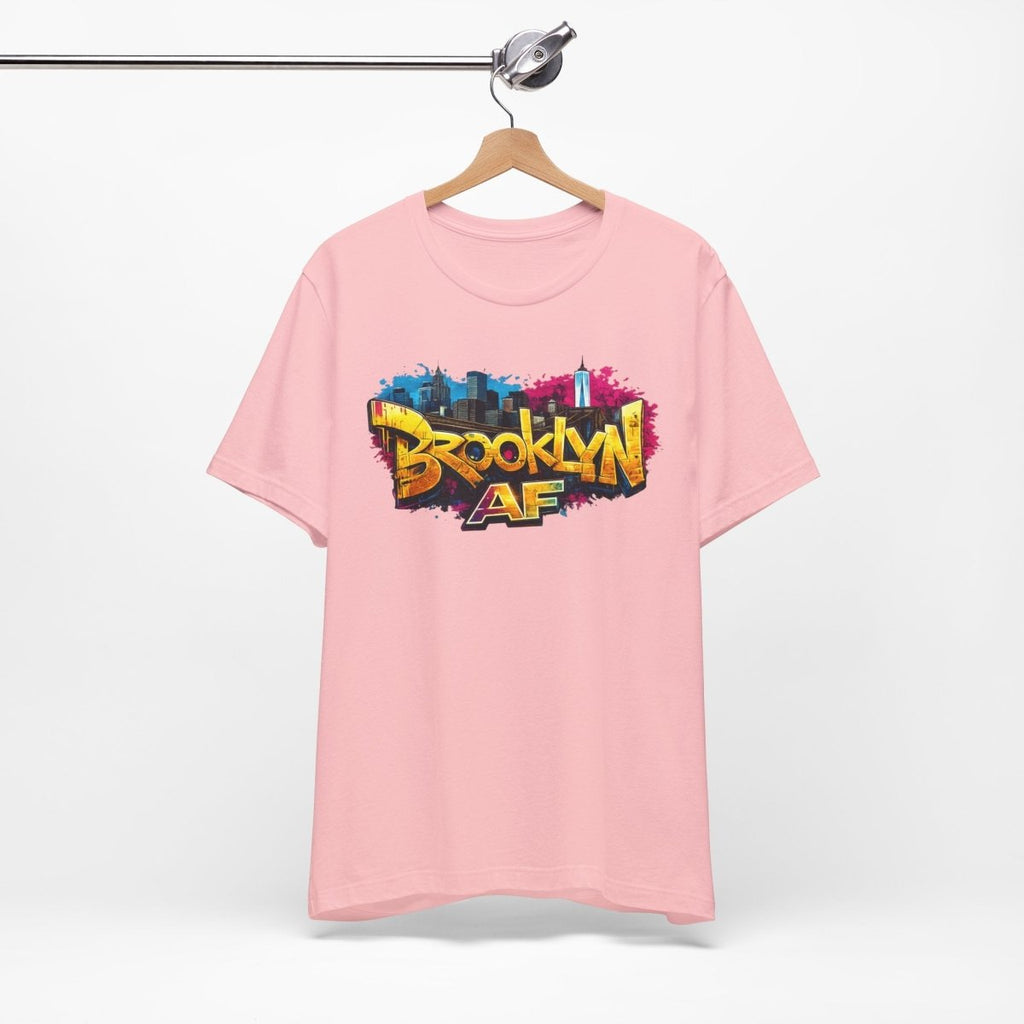 Pink Brooklyn AF graffiti tee on a wooden hanger against a white wall