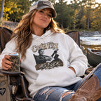 Woman in a camp chair by a river wearing the White Country As Fuck hoodie
